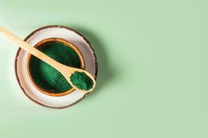 Natural Organic Spirulina Green Algae Powder in a wooden bowl and spoon on a ceramic plate. Top view. green background. A copy space. Detox. photo