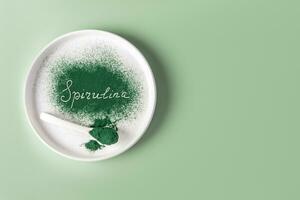 Spirulina inscription on green sprinkled spirulina powder on a white ceramic plate. Product presentation. A copy space. Natural food supplements. photo