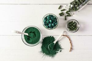 Round blue-green natural spirulina algae tablets and powder in bowl on white background. medical jar with seaweed capsules. Natural food supplements. photo