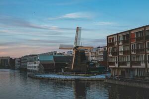 histórico molino en el bancos de un canal en uno de Holanda más hermosa ciudades, Amsterdam. paisaje de el ciudad durante puesta de sol foto