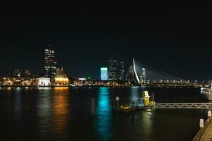 ver de el canal y el opuesto iluminado banco con un montón de iluminado rascacielos durante tarde noche en rotterdam, Países Bajos foto