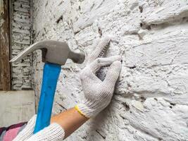 man is hitting nails with a hammer on a white brick wall and wearing white gloves photo