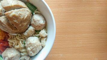a bowl of meatballs with additional noodles and vegetables on a table with wooden texture photo