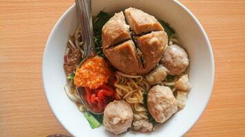 a bowl of meatballs with additional noodles and vegetables and with a spoonful of chili sauce photo