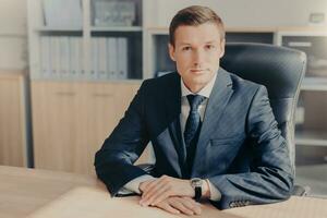 Serious businessman in suit using smartphone in sunlit office photo