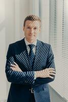 Confident businessman in a suit stands with crossed arms photo