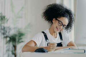 Joyful young student writing in notebook with a bright smile photo