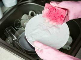 Woman's hands in rubber gloves hold a soapy kitchen sponge and a plate. Close-up. Selective focus. photo