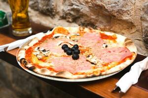 Delicious pizza with prosciutto, mushrooms, tomato paste and olives in a outdoor cafe. Selective focus. Close-up. photo