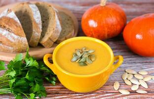 Delicious pumpkin cream soup and baked homemade bread on a wooden background. Close-up. photo