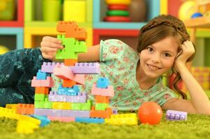 retrato de linda niña jugando con vistoso el plastico bloques en habitación foto