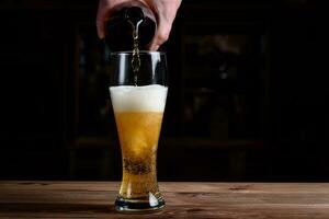 vaso con cerveza en un de madera mesa. cerveza es vertido dentro un vaso desde un botella. foto