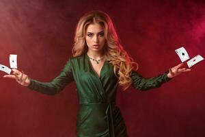 Blonde curly girl, make-up, in green dress and jewelry. Holding or showing something, posing on colorful smoky background. Copy space, close up photo