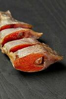 Slices of salted air-dried roach with roe on black wooden table photo