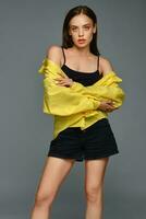 Confident young girl in black shorts and yellow shirt on grey background photo