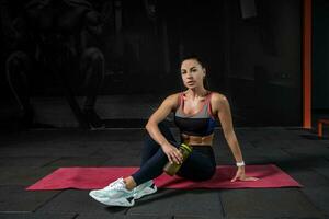 atlético joven mujer sentado en estera en moderno gimnasio foto