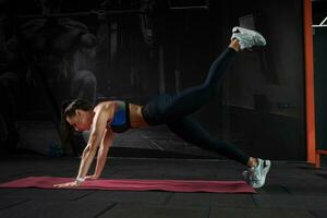 Girl performing front plank on straight arms with leg raises at gym photo