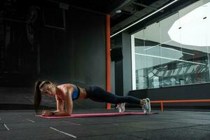 Young brunette standing in plank pose on elbows at gym photo