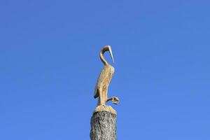 Figure of crane on the stump of a tree against the blue sky. Fig photo