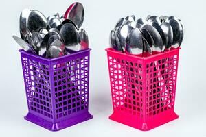 Stack of metal spoons in pink and purple plastic basket isolated on white background photo