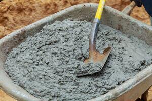 Worker shovels a wet mix of concrete from wheelbarrow at curb block installation. photo