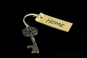 Old decorative key and handwritten tag HOME tied with straw rope on black background photo