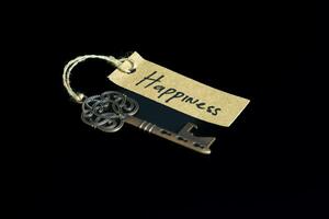 Old decorative key and handwritten tag Happiness tied with straw rope on black background photo