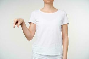 estudio Disparo de joven hembra vestido en blanco camiseta demostración letra q con su dedos mientras aprendizaje sordo alfabeto, aislado terminado blanco antecedentes foto