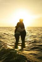 Silhouette of couple hugging on the beach with beautiful sunset in background. photo