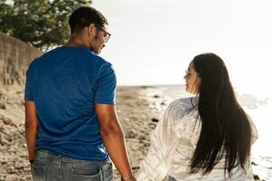 Young interracial couple holding hands at beach sunset. photo