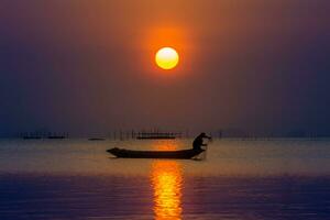 silueta pescador y puesta de sol cielo en el lago en sur de tailandia foto
