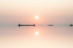 Mirror image of silhouette fisherman with sunset sky on the lake. photo