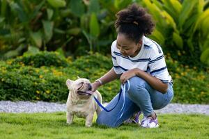 africano americano mujer es jugando con su francés buldog perrito mientras acostado abajo en el césped césped después teniendo Mañana ejercicio en el público parque foto