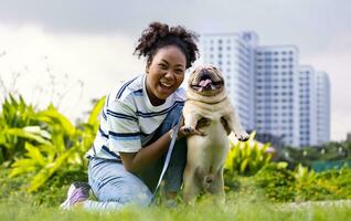 African American woman is playing with her french bulldog puppy while lying down in the grass lawn after having morning exercise in the public park photo
