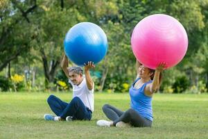 Senior asian man and his daughter are exercising with yoga ball in the public park to build core body muscle for elder longevity exercise and outdoor workout photo