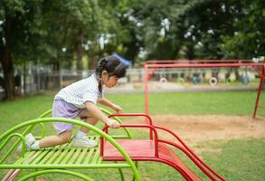 Cute asian girl smile play on school or kindergarten yard or playground. Healthy summer activity for children. Little asian girl climbing outdoors at playground. Child playing on outdoor playground. photo