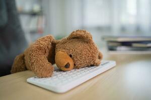 Brown teddy bear sitting on a desk Lying down looks tired on the white keyboard. depression sad concept. photo