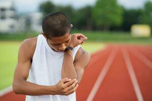 Athletes sport man runner wearing white sportswear to sitting feeling pain in his elbow after practicing on a running track at a stadium, copy space. Runner sport injury concept. photo