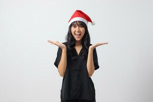Portrait of excited Asian woman with red Santa hat spreading hands, showing product, choosing between two different option. New year and christmas concept. Isolated image on white background photo