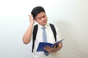 Indonesian senior high school student wearing white shirt uniform with gray tie writing on note book using pen with annoyed and frustrated expression. Isolated image on white background photo