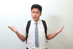 confuso mayor alto colegio estudiante vistiendo blanco camisa uniforme con gris Corbata extensión su manos oblicuo y participación dos cosas, demostrar productos aislado imagen en blanco antecedentes foto