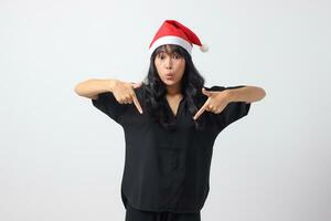 Portrait of attractive Asian woman with red Santa hat feeling happy, showing and pointing down with finger. New year and christmas concept. Isolated image on white background photo