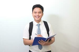 Indonesian senior high school student wearing white shirt uniform with gray tie writing on note book using pen. Isolated image on white background photo