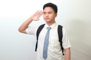 indonesio mayor alto colegio estudiante vistiendo blanco camisa uniforme con gris Corbata dando saludo actitud con mano durante bandera ceremonia. aislado imagen en blanco antecedentes foto