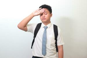 Indonesian senior high school student wearing white shirt uniform with gray tie suffering headache and holding hands on forehead. Isolated image on white background photo