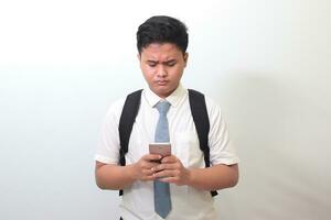 Indonesian senior high school student wearing white shirt uniform with gray tie showing confusion face expression while holding a mobile phone. Isolated image on white background photo
