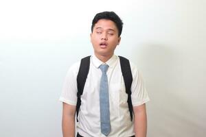 Indonesian senior high school student wearing white shirt uniform with gray tie yawning with closed eyes due to overworking. Isolated image on white background photo