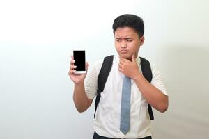 indonesio mayor alto colegio estudiante vistiendo blanco camisa uniforme con gris Corbata demostración y presentación blanco pantalla móvil teléfono. aislado imagen en blanco antecedentes foto