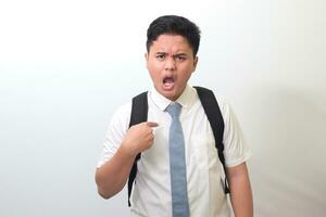 Indonesian senior high school student wearing white shirt uniform with gray tie direct finger own chest listen unfair blaming saying it's not me. Isolated image on white background photo