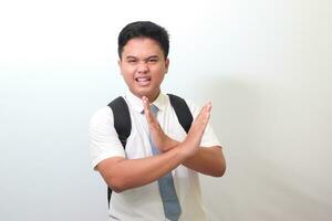 Indonesian senior high school student wearing white shirt uniform with gray tie showing X sign of hands. Teenager refusing an invitation from someone. Isolated image on white background photo